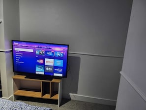 Un televisor sobre un soporte de madera en una habitación con pared y alfombra blancos.