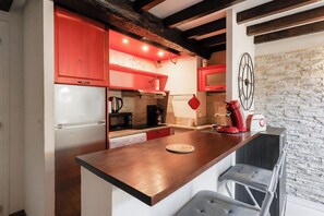 A kitchen with a wooden island, red cabinets, a stone wall, and a vintage radio. - Upstays Lions Duplex 45m² Suquet Port (Cannes)