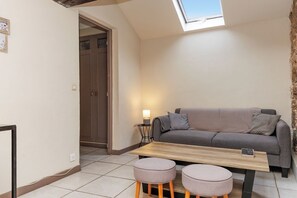 A small, cozy room with a sofa, a table, and two ottomans. There's a door leading to another room and a skylight above the sofa. - Upstays Lions Duplex 45m² Suquet Port (Cannes)