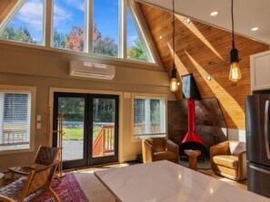 A spacious living area with a high ceiling, large windows, a fireplace, and modern furniture.