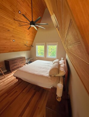 A bedroom with a sloped ceiling, a bed, a dresser, and two windows.