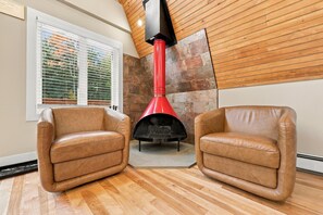 A room with two leather armchairs, a stone wall, a red chimney, and a window with blinds.