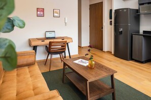 A compact living space with a sofa, a wooden dining table with a vase, a laptop on a desk, a refrigerator, and a door. - Contemporary Escape in Roma Norte (Mexico City)