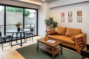 Ein modernes Wohnzimmer mit einer Couch, einem Couchtisch, einem Esstisch mit Stühlen und einem großen Fenster.