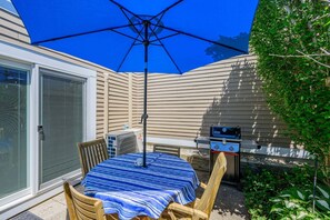 Eine Terrasse mit Tisch, Stühlen, einem Grill und einem Sonnenschirm.