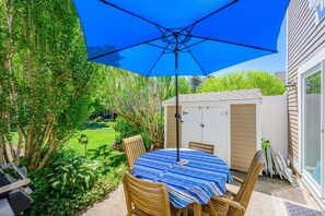 Eine Terrasse mit einem runden Tisch, Stühlen und einem blauen Sonnenschirm.