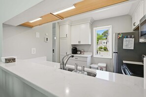 A modern kitchen with white cabinetry, a stainless steel sink, and a window overlooking a residential area. - Brewster townhouse near beach & golf (Brewster)