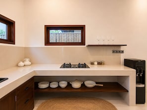 Eine moderne Küche mit Gasherd, weißen Schränken, einem kleinen Fenster und einem Regal mit Gläsern.