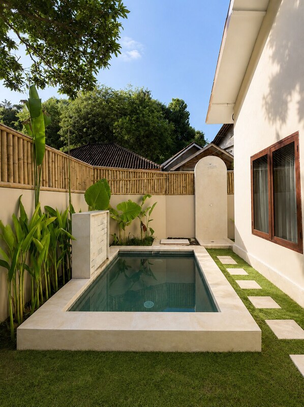 A swimming pool surrounded by a bamboo fence, with a small garden area and a building with a tiled roof.