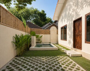 A courtyard with a swimming pool, a wooden fence, and a building with a door and window.