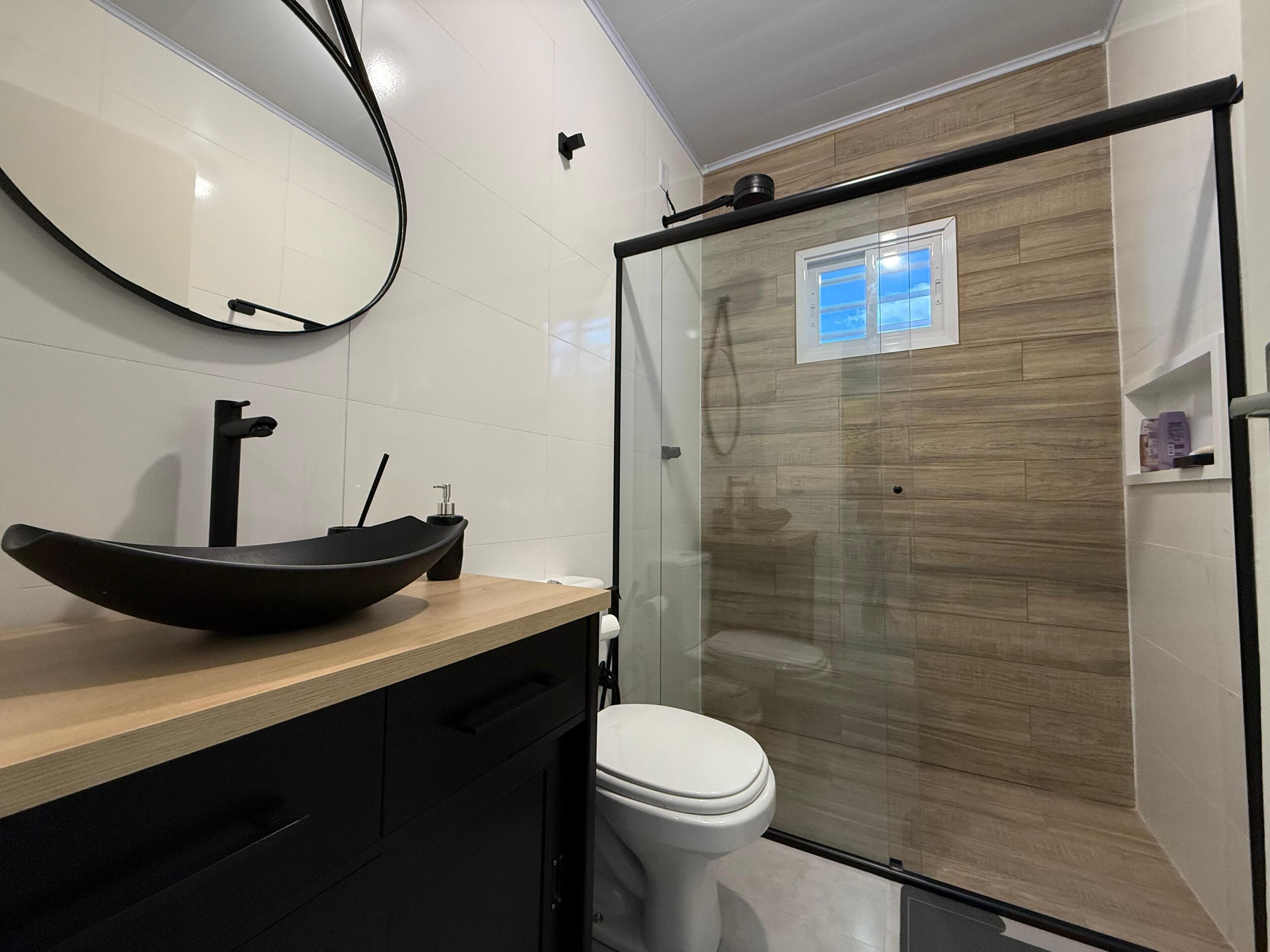 A modern bathroom with a black vessel sink, a white toilet, and a glass shower enclosure.