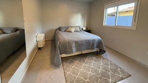 A bedroom with a bed, bedside table, nightstand, window, and a rug.