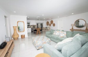 Ein modernes Wohnzimmer mit einer Couch, einem Hocker und einem Essbereich im Hintergrund.