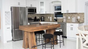Una cucina moderna con mobili bianchi, elettrodomestici in acciaio inossidabile, un piano di lavoro in granito e un'isola in legno con sgabelli da bar.