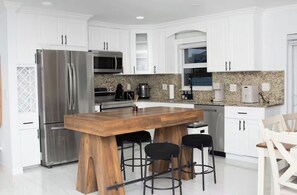 Eine moderne Küche mit weißen Schränken, Edelstahlgeräten, einer Granitarbeitsplatte und einer Holztheke mit Barhocker.