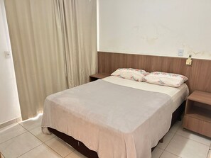 Une chambre à coucher avec un lit, des tables de chevet, une tête de lit en bois, un rideau et une prise électrique murale.