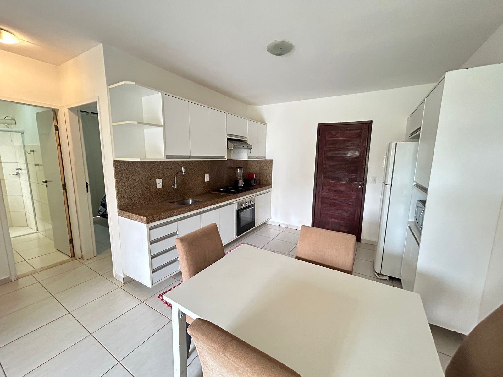 A compact kitchen with white cabinets, a granite countertop, a built-in oven, and a refrigerator.