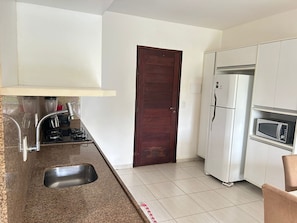 Eine kompakte Küche mit eingebautem Gaskochfeld, Spüle, Mikrowelle und Kühlschrank.