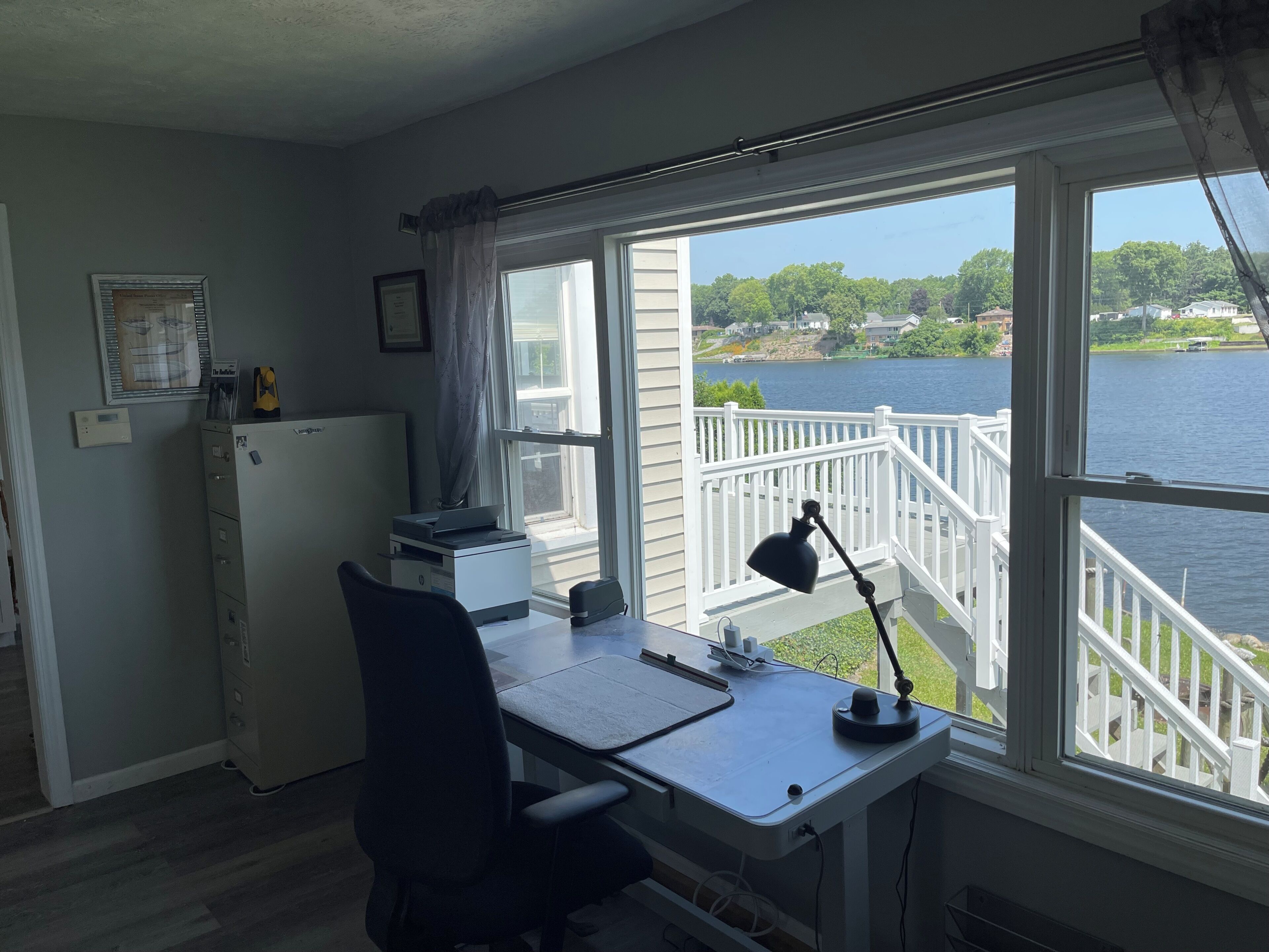 A room with a desk, chair, printer, and a view of a lake through a window.