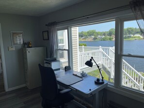 A room with a desk, chair, printer, and a view of a lake through a window.