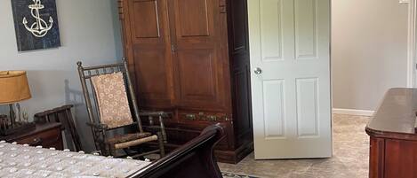 Un dormitorio con cama, una silla, un armario, una puerta y una alfombra.
