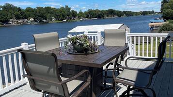 A deck with a table and chairs overlooking a lake, surrounded by a white railing.
