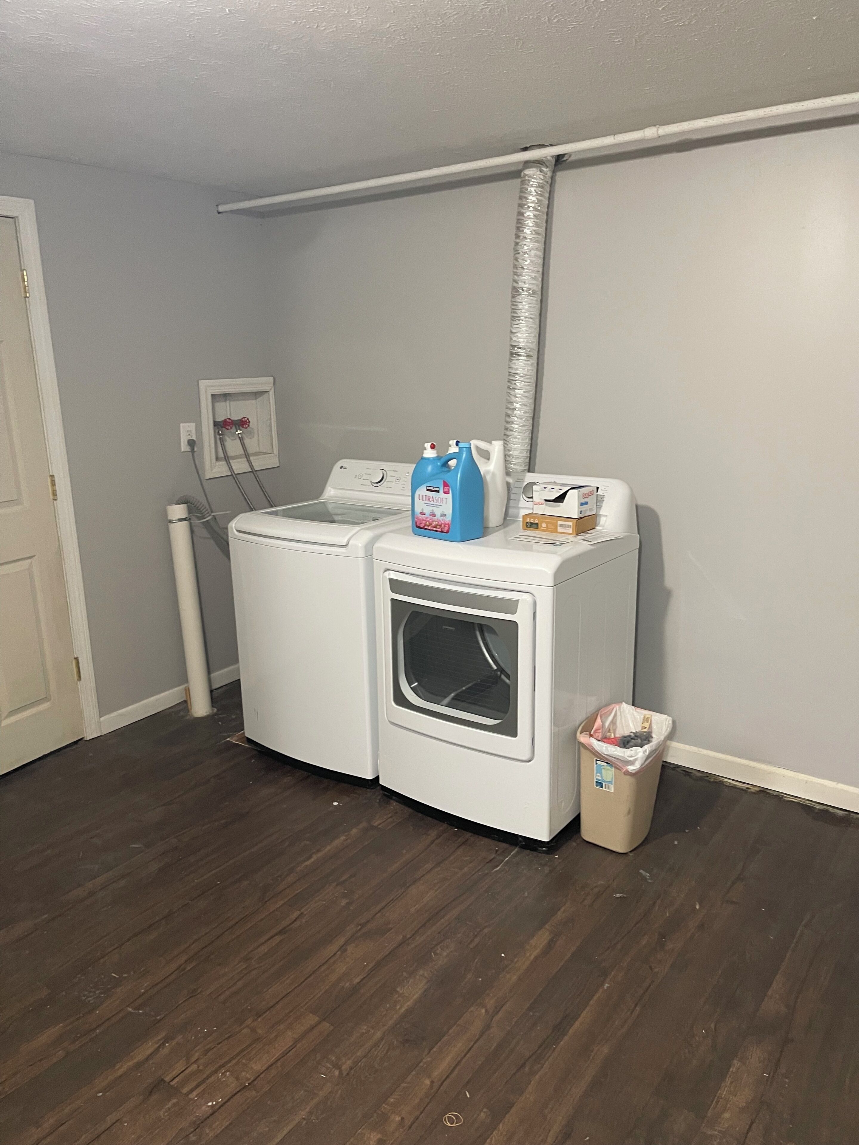 A laundry area with a front-loading washer and dryer, a trash can, and a laundry detergent bottle.