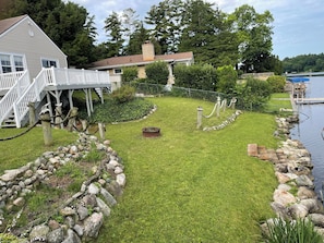 Une pelouse bien entretenue, bordée de pierres, avec une terrasse en bois et un quai s’avançant dans un lac.