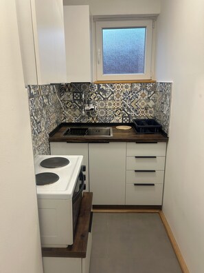 A compact kitchen with a stove, sink, and window. - Affordable Cozy Apartment in Skopje (Skopje)