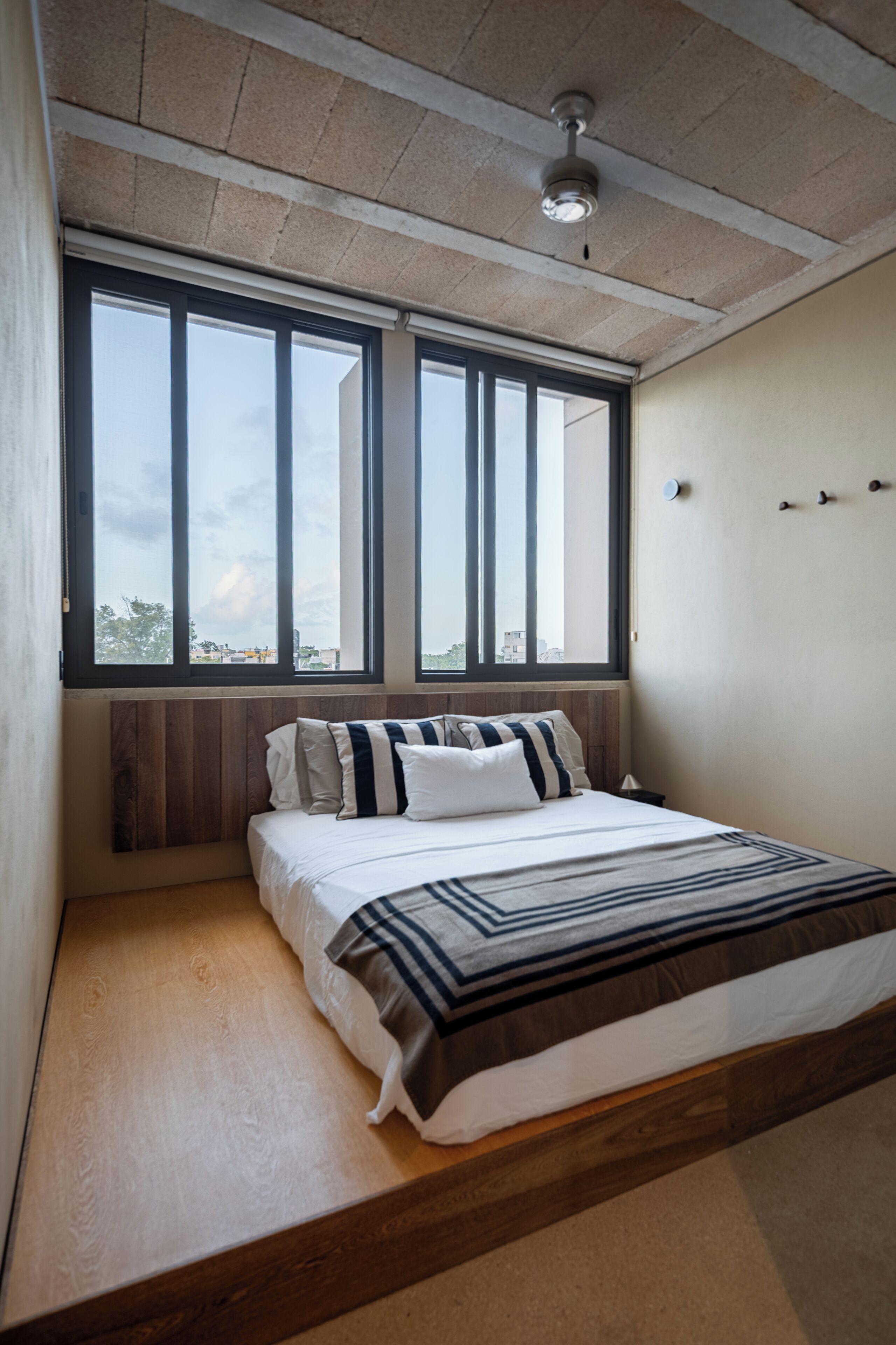 A bedroom with a bed, large windows, a ceiling fan, and a view of the sky.