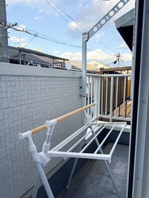 Ein Balkon mit weißem Metallgeländer, einem hölzernen Handtuchhalter und einer Ziegelwand.