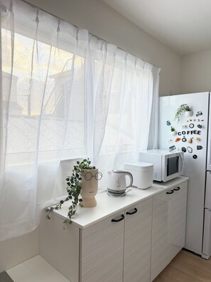 Eine moderne Küche mit weißer Arbeitsplatte, einem Wasserkocher, einer Mikrowelle und einem Kühlschrank.