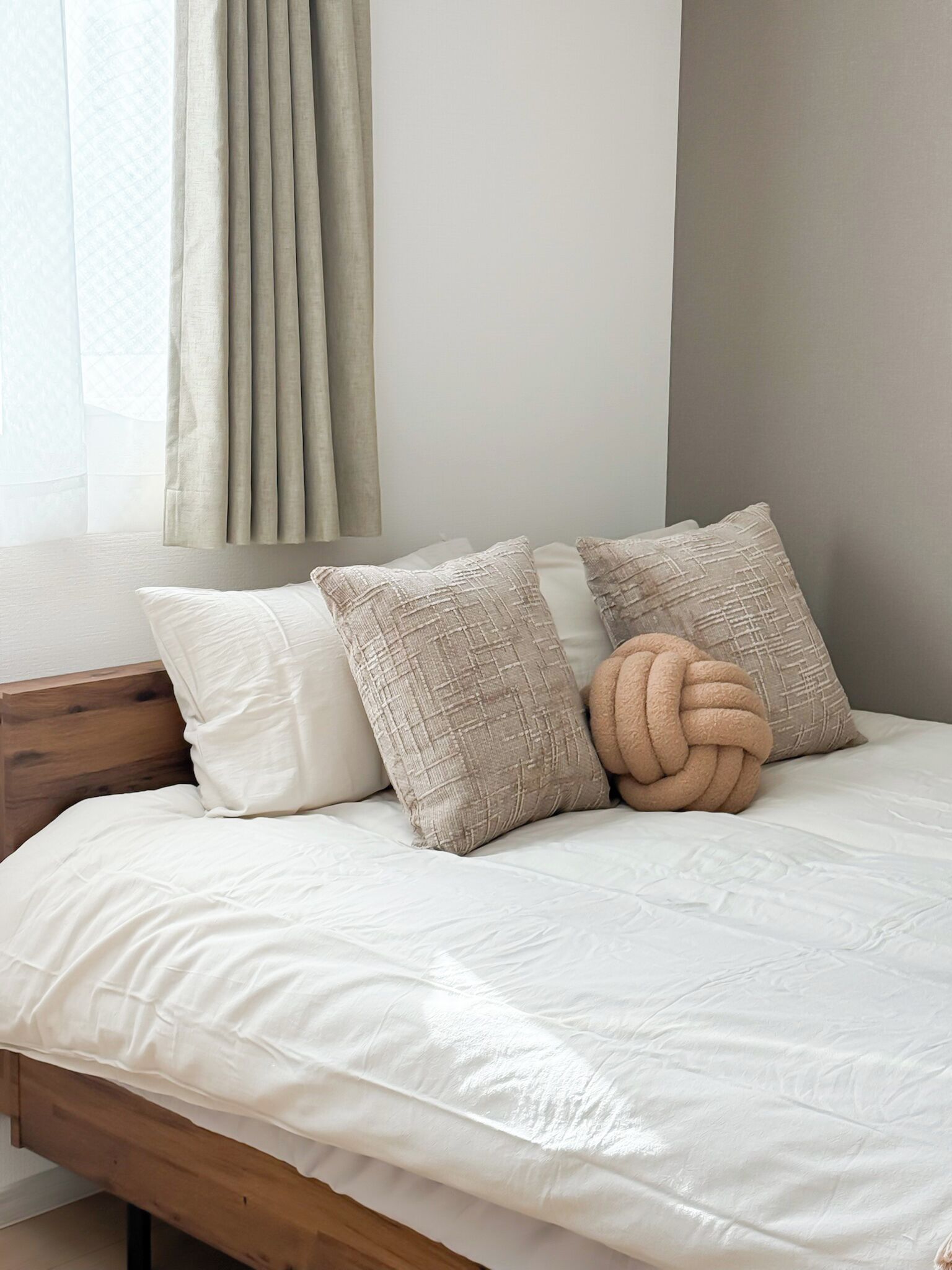 A bed with white bedding, two beige pillows, and a textured throw pillow.
