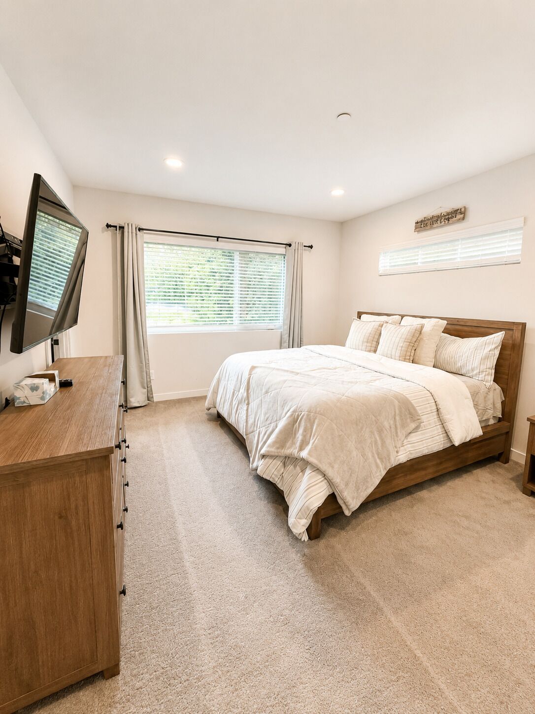 Une chambre à coucher avec un lit, un bureau, une télévision et une fenêtre avec des rideaux.