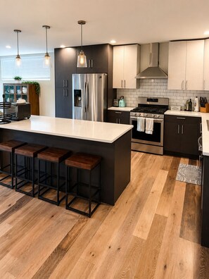 A modern kitchen with a central island, stainless steel appliances, and wooden flooring.
