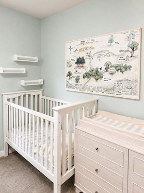 A baby room with a crib, dresser, and a wall map.