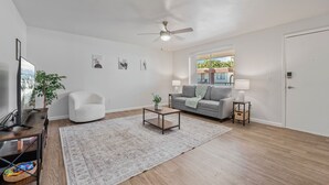 A living room with a ceiling fan, a gray sofa, a white armchair, a coffee table, and a TV on a wooden stand. - Bright Mesa Getaway Near Dining and Shopping (Mesa)