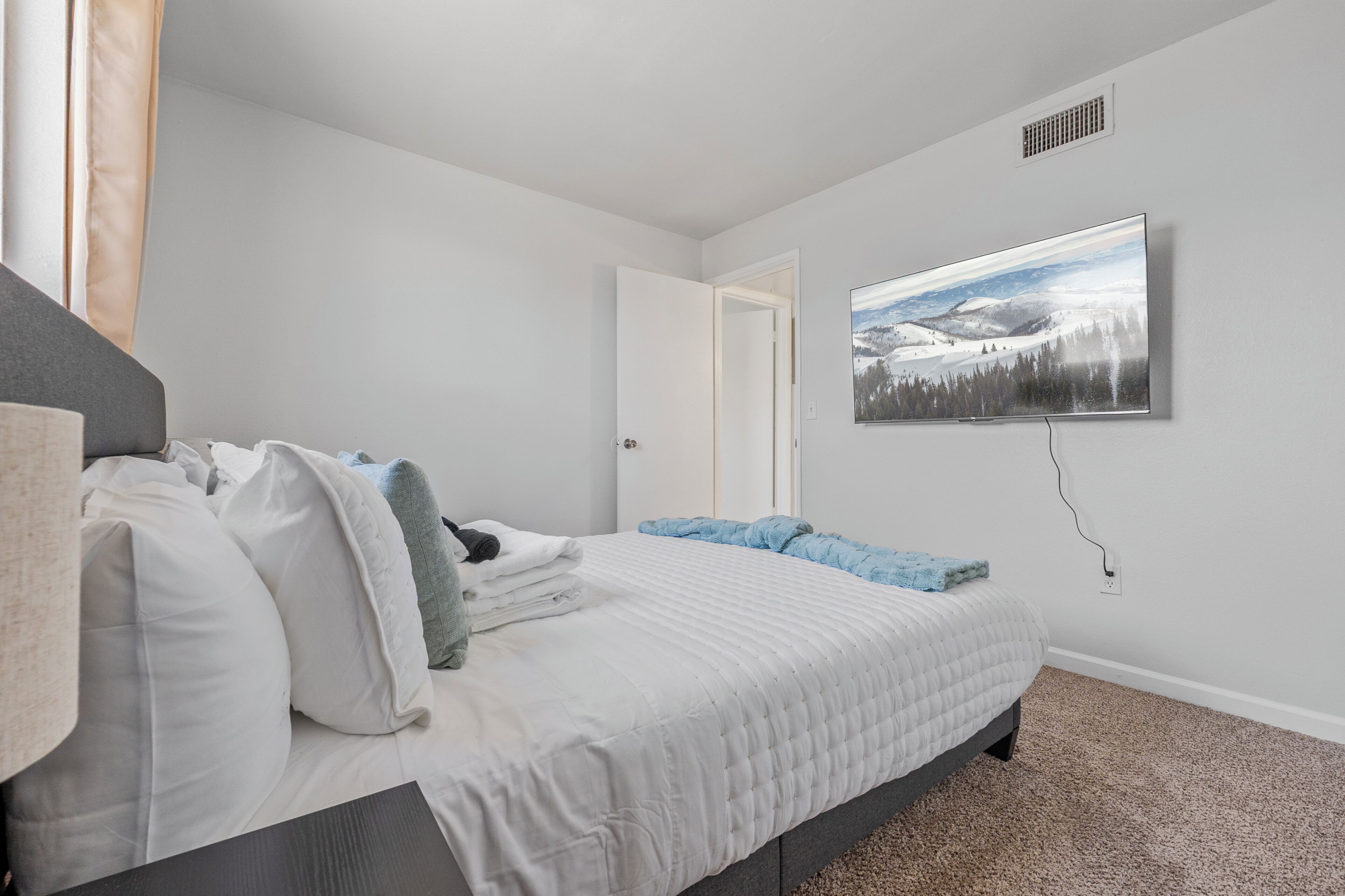 Une chambre à coucher avec un lit, un téléviseur fixé au mur et une porte donnant sur une autre pièce.