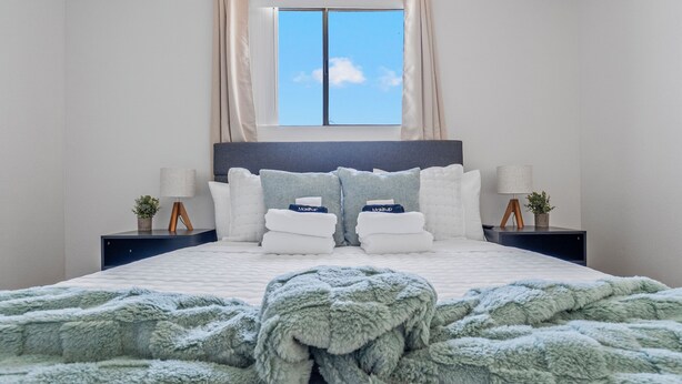 A neatly made bed with a fluffy green blanket, a headboard, and two bedside tables with lamps and small potted plants. - Bright Mesa Getaway Near Dining and Shopping (Mesa)