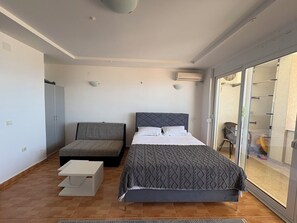 Ein Schlafzimmer mit Bett, einer Couch, einem kleinen Tisch und einer Schiebeglastür zum Balkon.