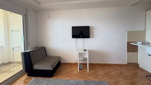 A modern living room with a sofa, a TV mounted on the wall, a small white table, and a kitchen area visible through an open door. - Perfect cozy apartment close to the Old town/Small beach/Women only beach (Ulcinj)