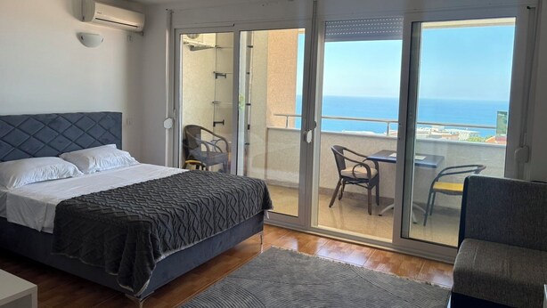 A bedroom with a bed, a small table, and a chair, a balcony with a view of the sea, and an air conditioning unit on the wall. - Perfect cozy apartment close to the Old town/Small beach/Women only beach (Ulcinj)