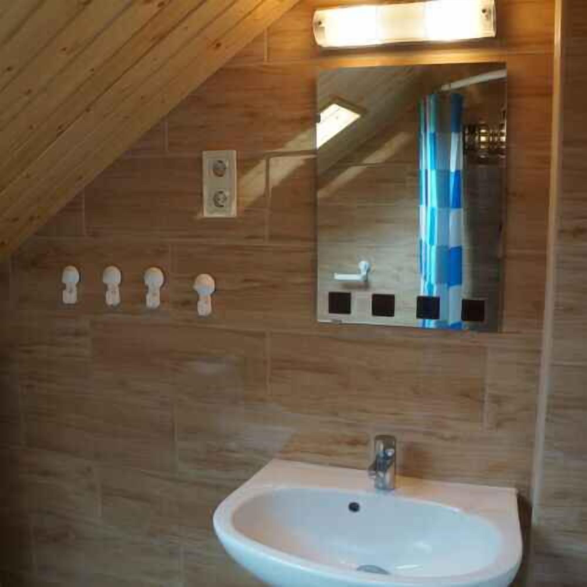 Une salle de bain avec un plafond en bois, un lavabo blanc, un miroir et un rideau de douche à rayures bleues et blanches.