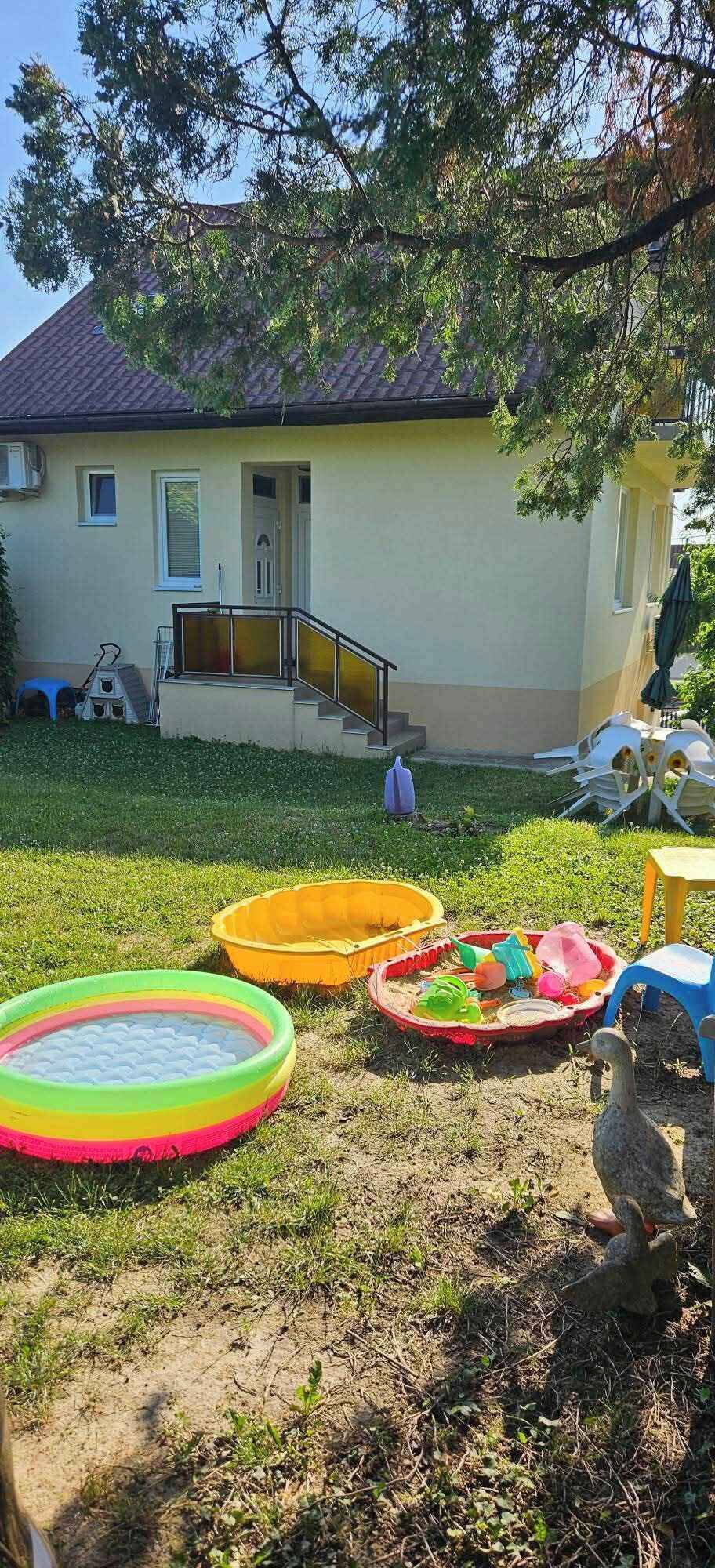 Une maison avec un jardin devant, où l’on trouve des piscines gonflables et une statue.