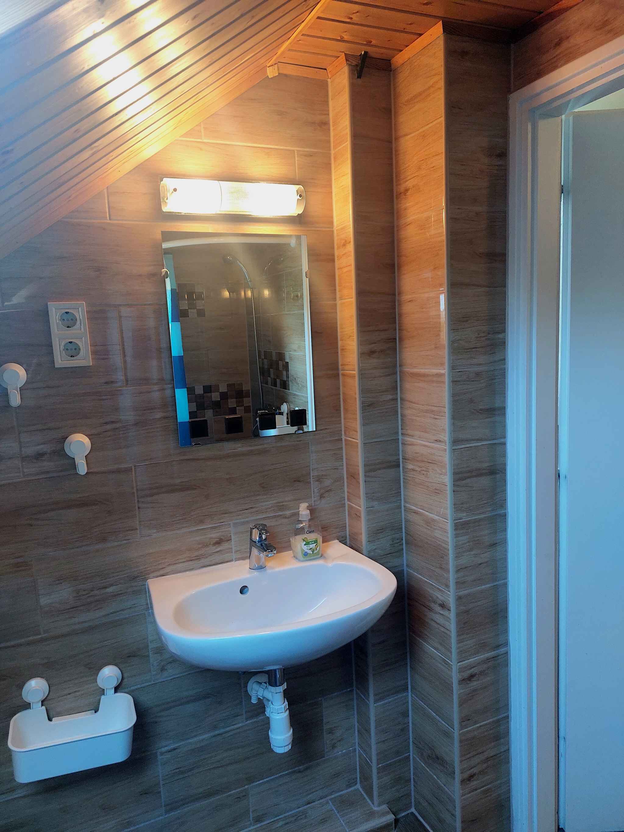 A bathroom with a wooden ceiling, a white sink, a mirror, and a shower.