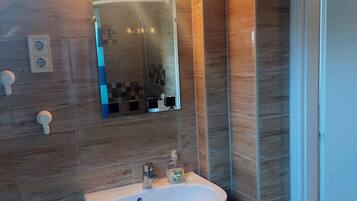 A bathroom with a wooden ceiling, a white sink, a mirror, and a shower.