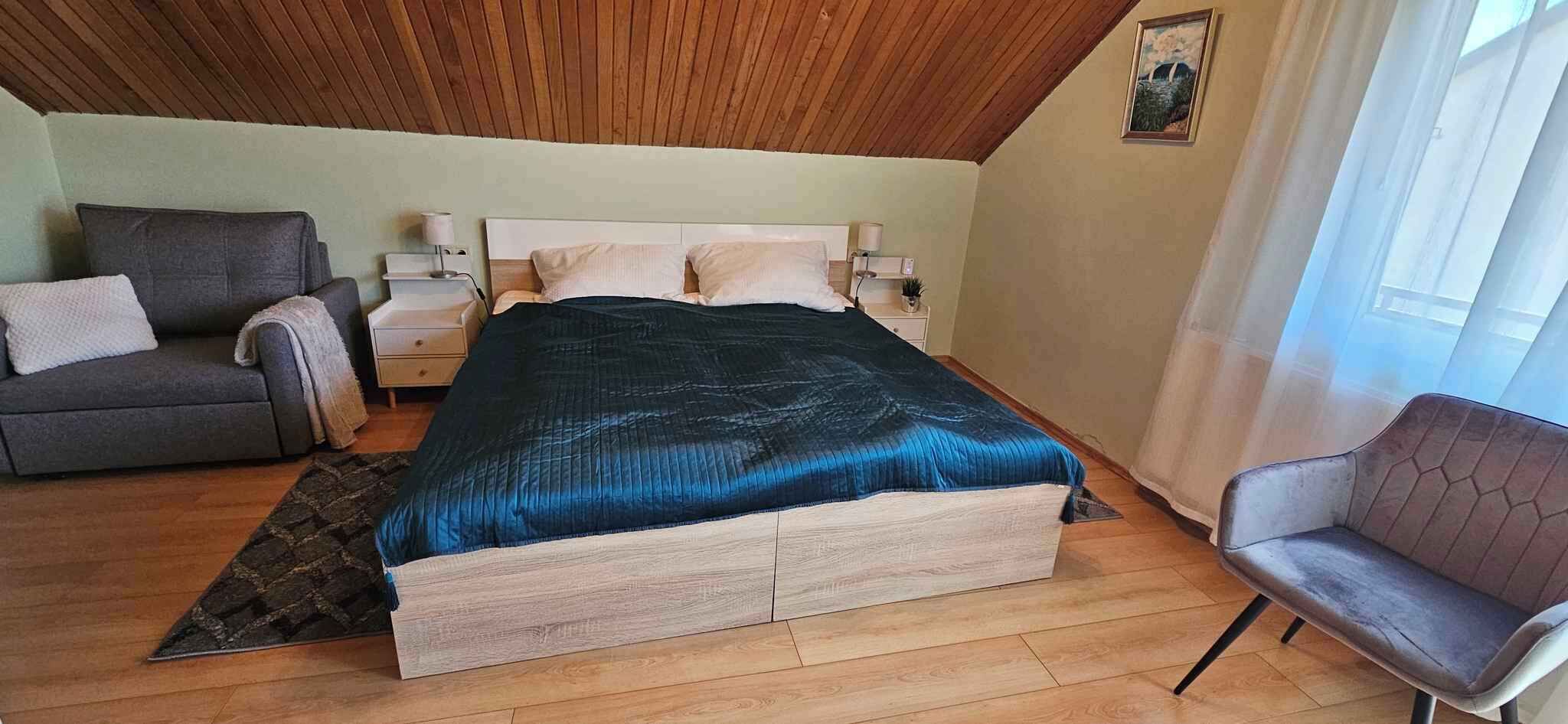 Een slaapkamer met een bed, een bank, een stoel, een nachtkastje en een schilderij aan de muur.
