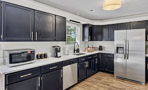 A modern kitchen with dark cabinetry, stainless steel appliances, and a white countertop.