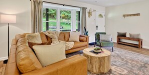 A living room with a leather sofa, a round wooden coffee table, and a view of a garden through large windows.