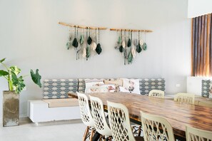 A dining area with a wooden table, white chairs, a sofa with patterned cushions, and macramé wall hangings. - Luxury Villa in Santa Fe de Antioquia (Casa Sereno) (San Nicolas)